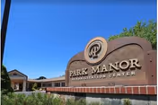 Outdoor view of the entrance sign for Park Manor Rehabilitation Center with a clear blue sky in the background and part of the building visible behind the sign.