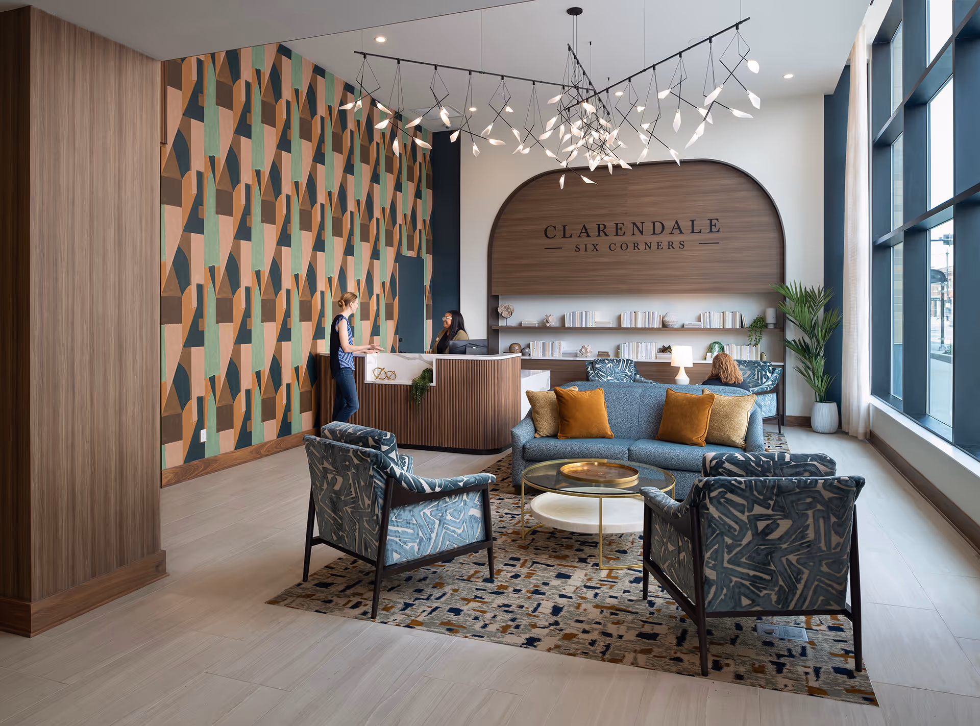 Reception lobby of Clarendale Six Corners with a seating area, patterned feature wall, and a front desk under a wood-arched sign.