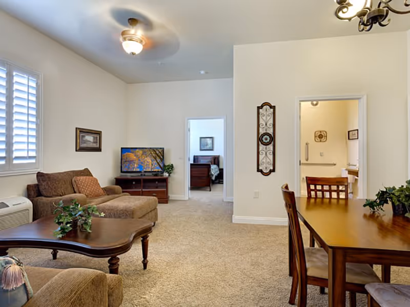 Bright furnished living and dining area with a sofa, coffee table, TV, and dining table opening to a bedroom and bathroom.