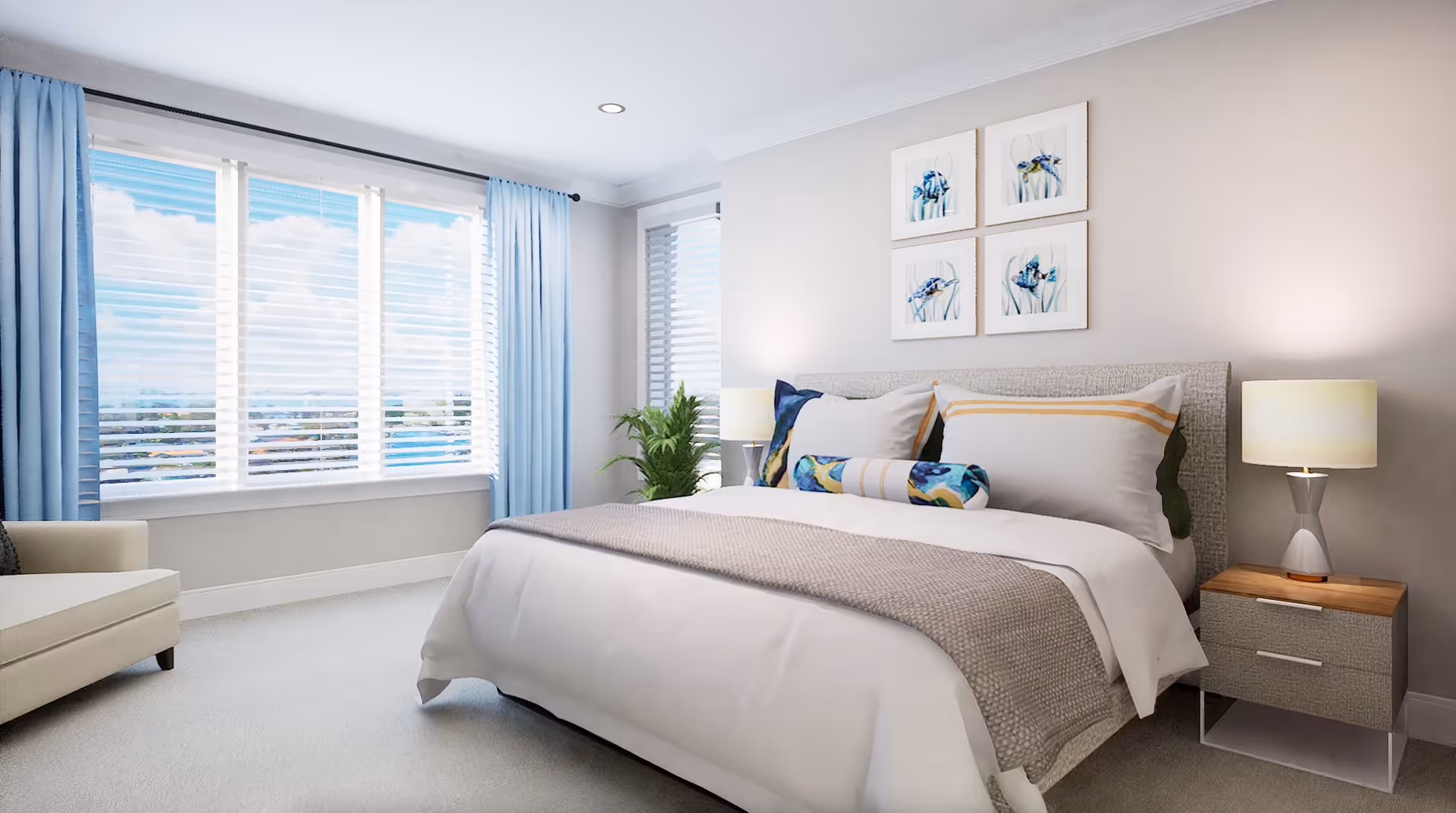 A bright and airy bedroom with a large bed featuring white and beige bedding, decorative pillows, and a throw blanket. There is a nightstand with a lamp on the right side of the bed, a beige armchair on the left, and large windows with white blinds and light blue curtains letting in natural light. Four framed pictures of fish hang on the wall above the bed, and a green plant is placed near the corner window.