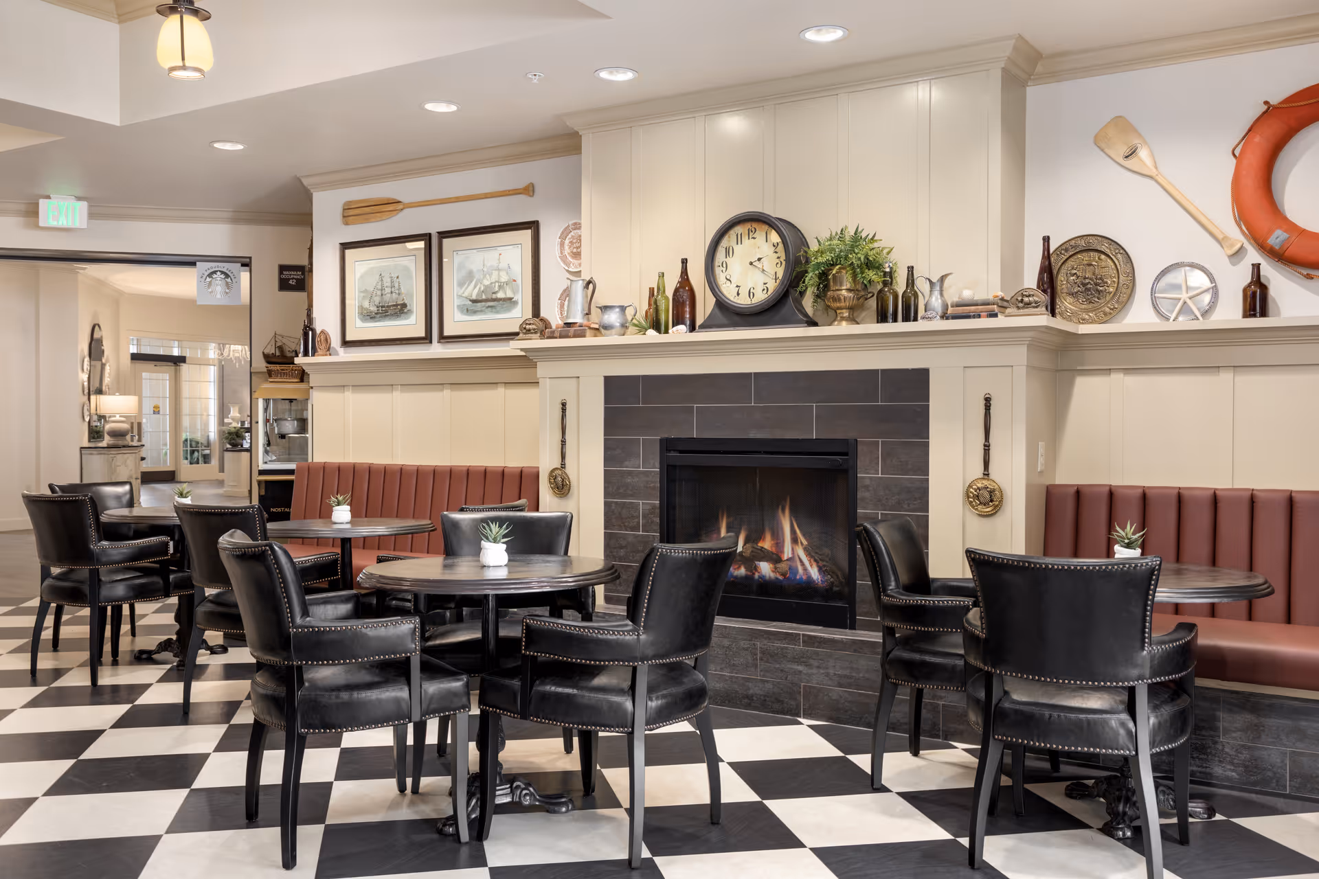 Cozy communal dining/lounge area with round tables and leather chairs facing a lit fireplace and nautical decor.