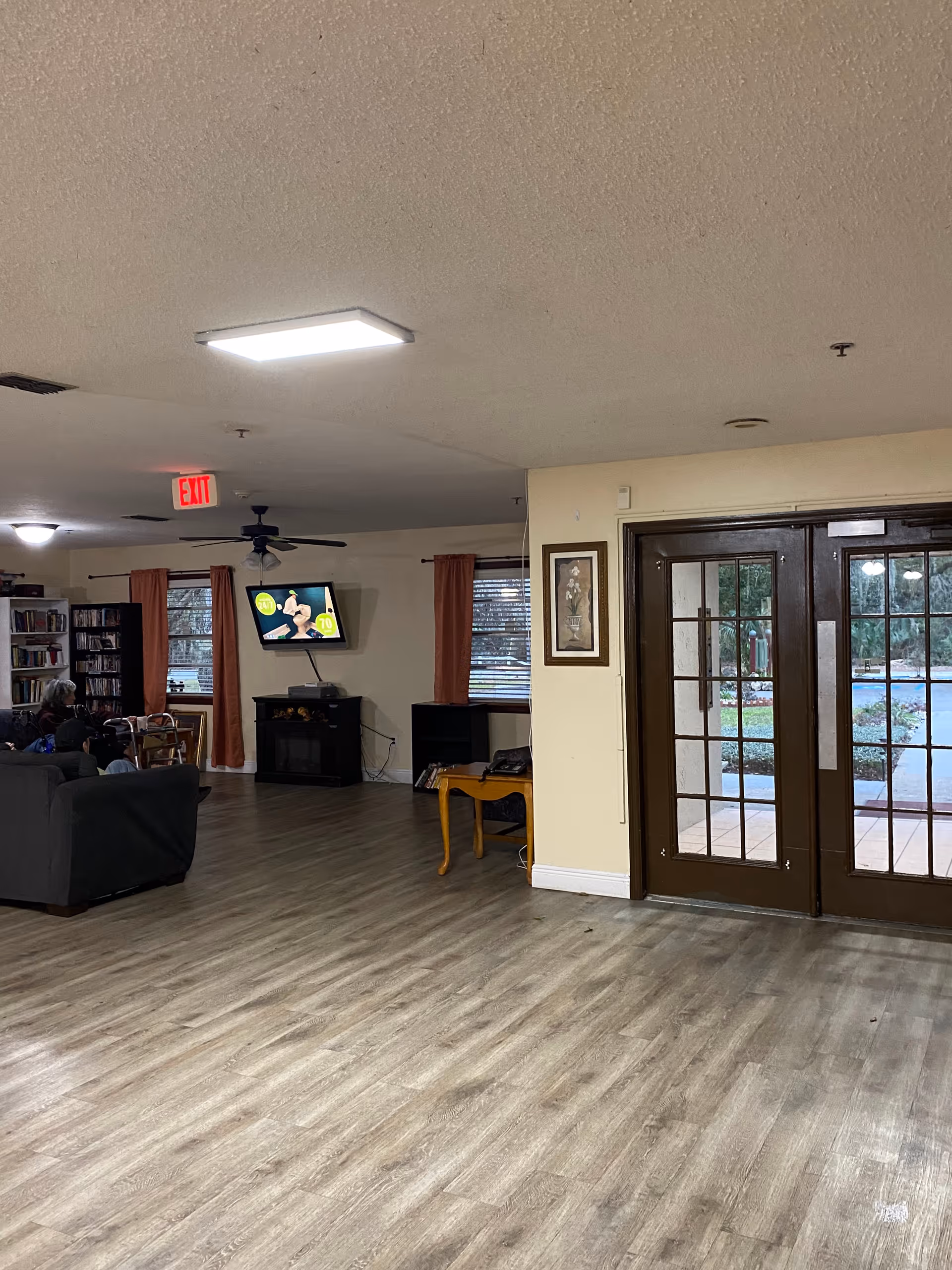 Communal living room with sofas, a wall-mounted TV, bookshelves, and glass double doors to the outside.