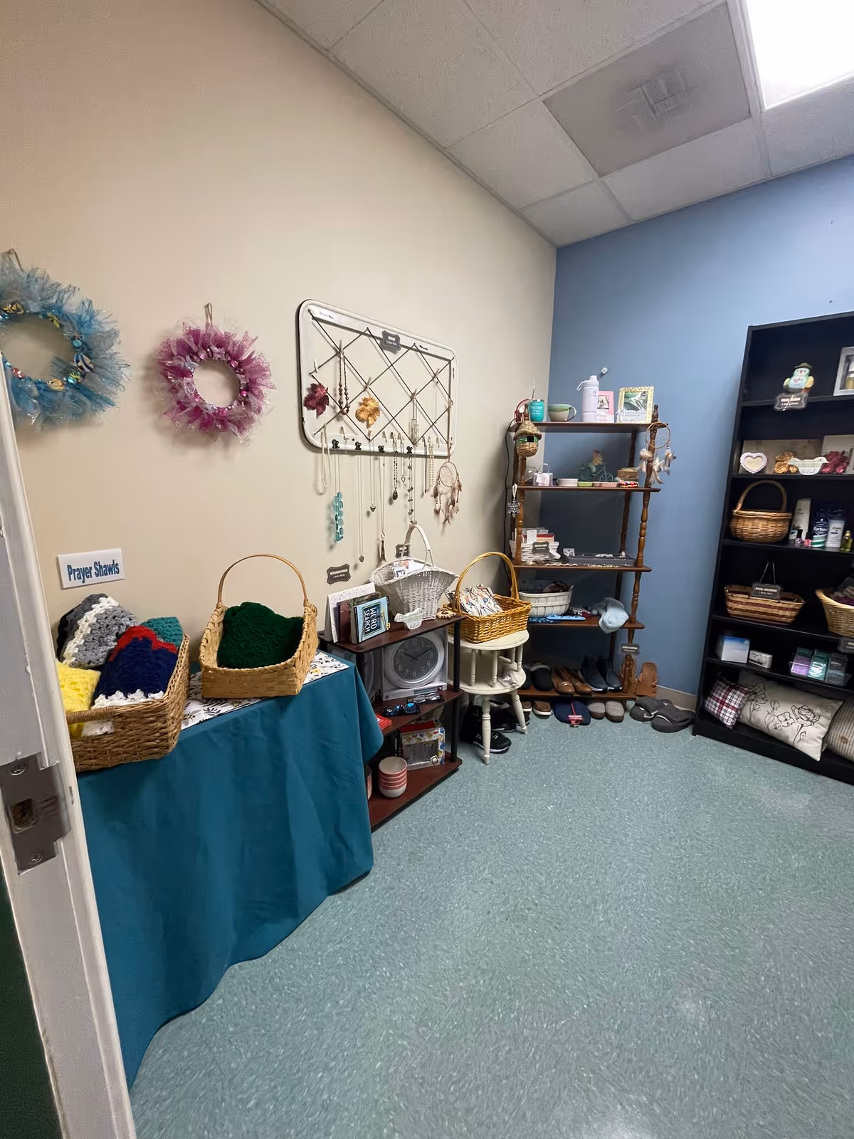 Small interior room with shelves, baskets of knitted prayer shawls and various gift items on display.
