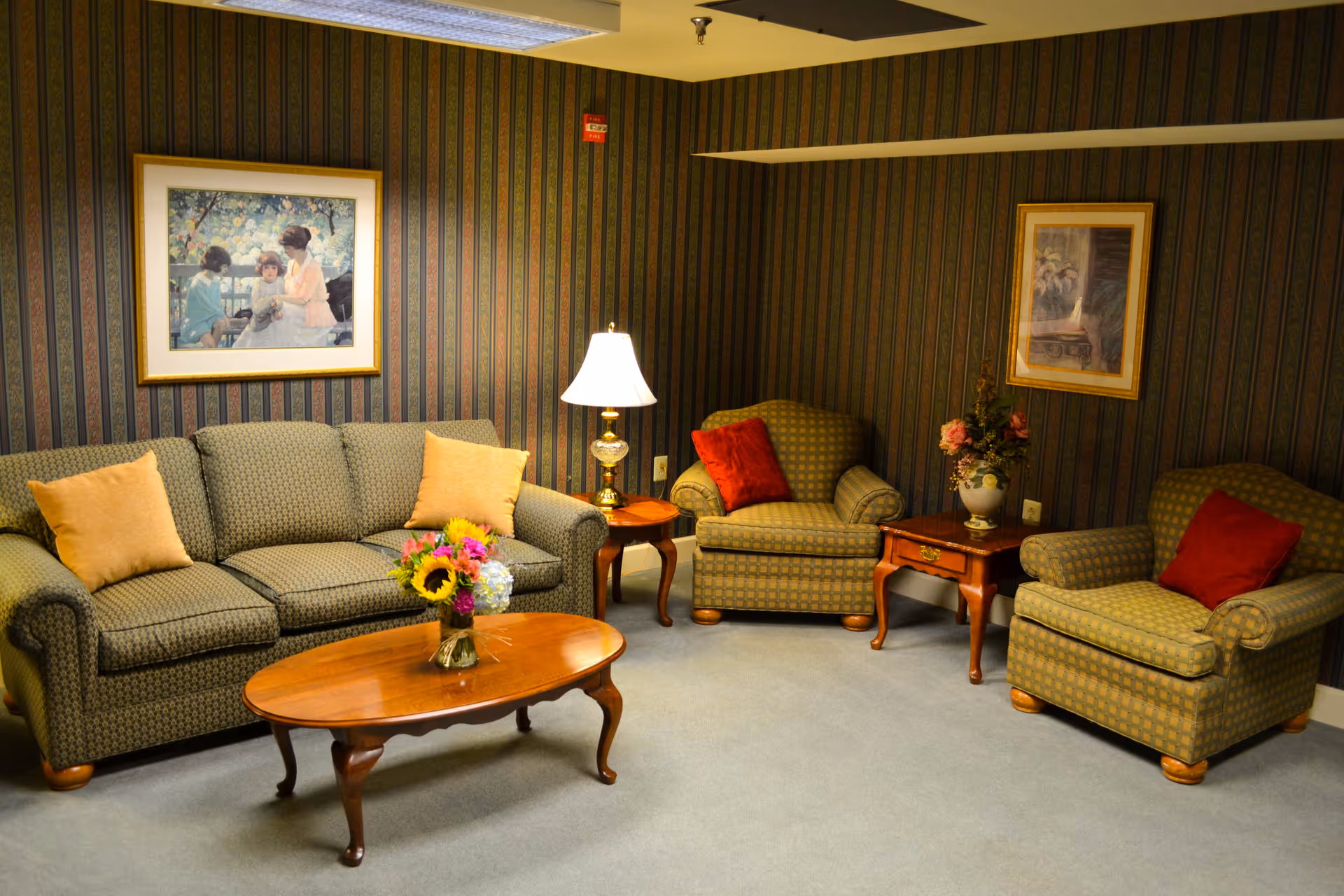 Cozy seating area with an upholstered sofa and three armchairs arranged around a wooden coffee table, side tables, a lamp, and floral arrangements.