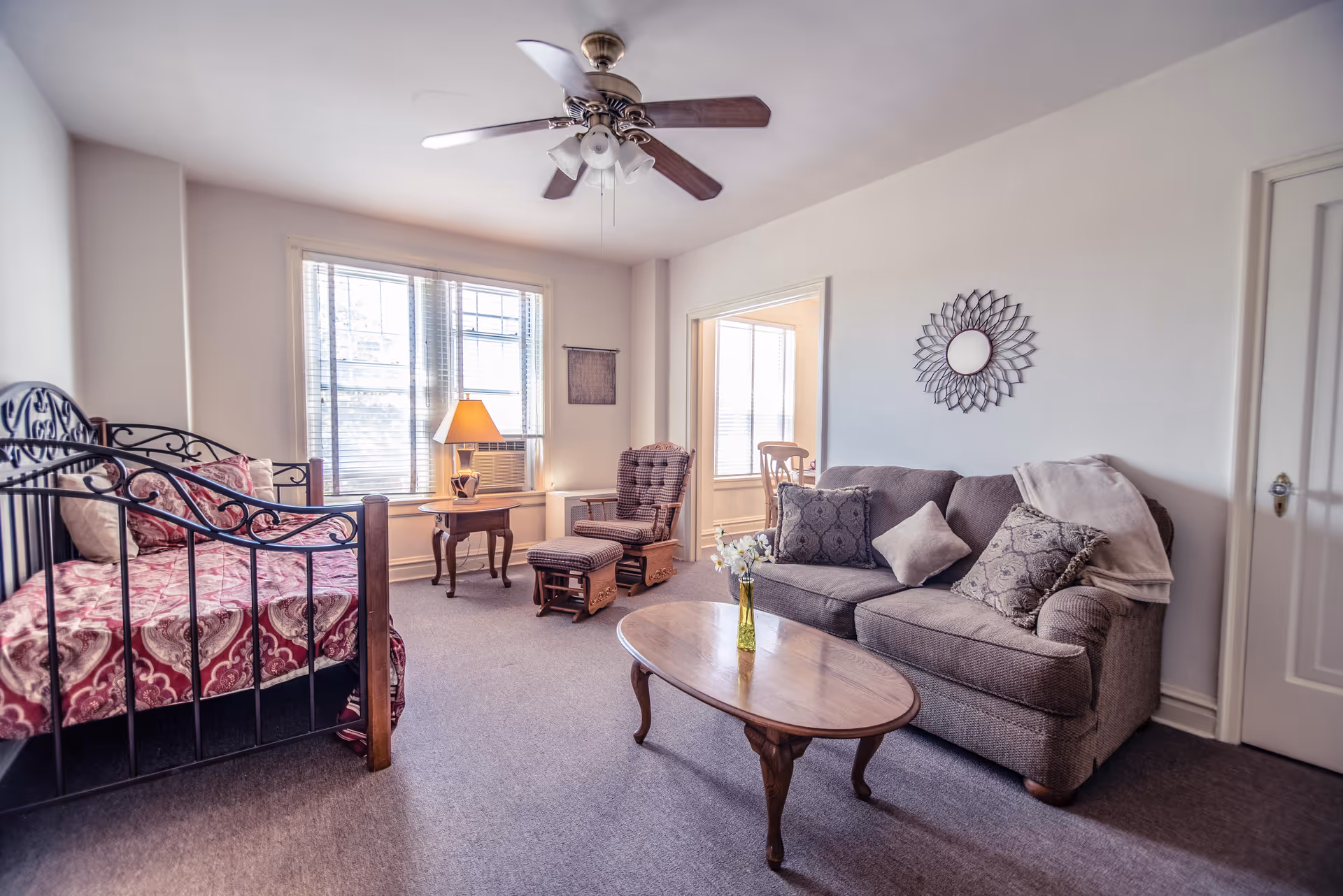 Bright, furnished living area with a sofa, coffee table, daybed, armchair, and ceiling fan near a window.