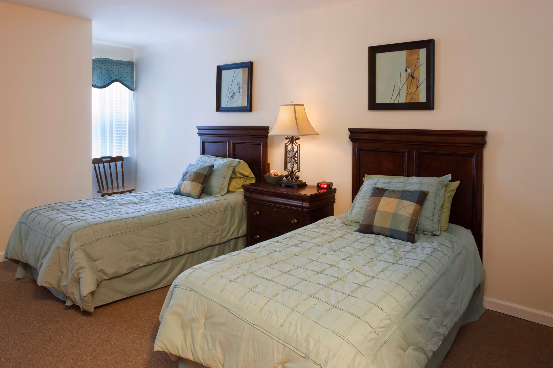 Twin-bed bedroom with two neatly made beds, a central nightstand and lamp, and framed artwork on the wall.