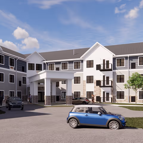 Exterior view of a three-story senior living facility building with a covered entrance. Several cars are parked in front, and a few people are walking near the entrance. The building has multiple windows and small balconies, with a clear blue sky above.