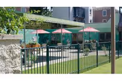 Outdoor courtyard with pink umbrellas, tables, and a black fence at a senior facility.