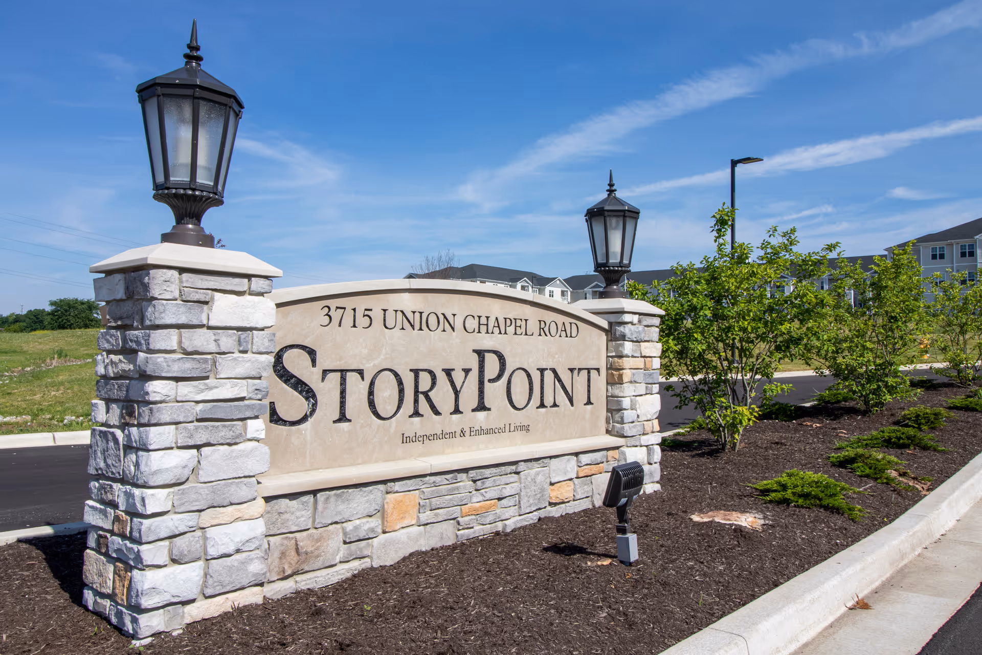 Stone entrance sign for StoryPoint at 3715 Union Chapel Road with two lantern-style lights on stone pillars, surrounded by landscaping and a clear blue sky.