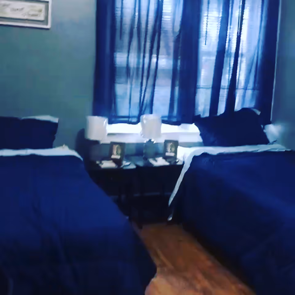 Two twin beds with blue bedding flanking a window and a small nightstand in a bedroom.