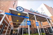 Exterior view of the entrance to Linden Center for Nursing and Rehabilitation, showing a covered walkway with blue signage and a flower logo above the facility name on the building.