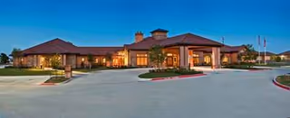 Wide exterior view of San Remo senior living facility with illuminated front entrance at dusk