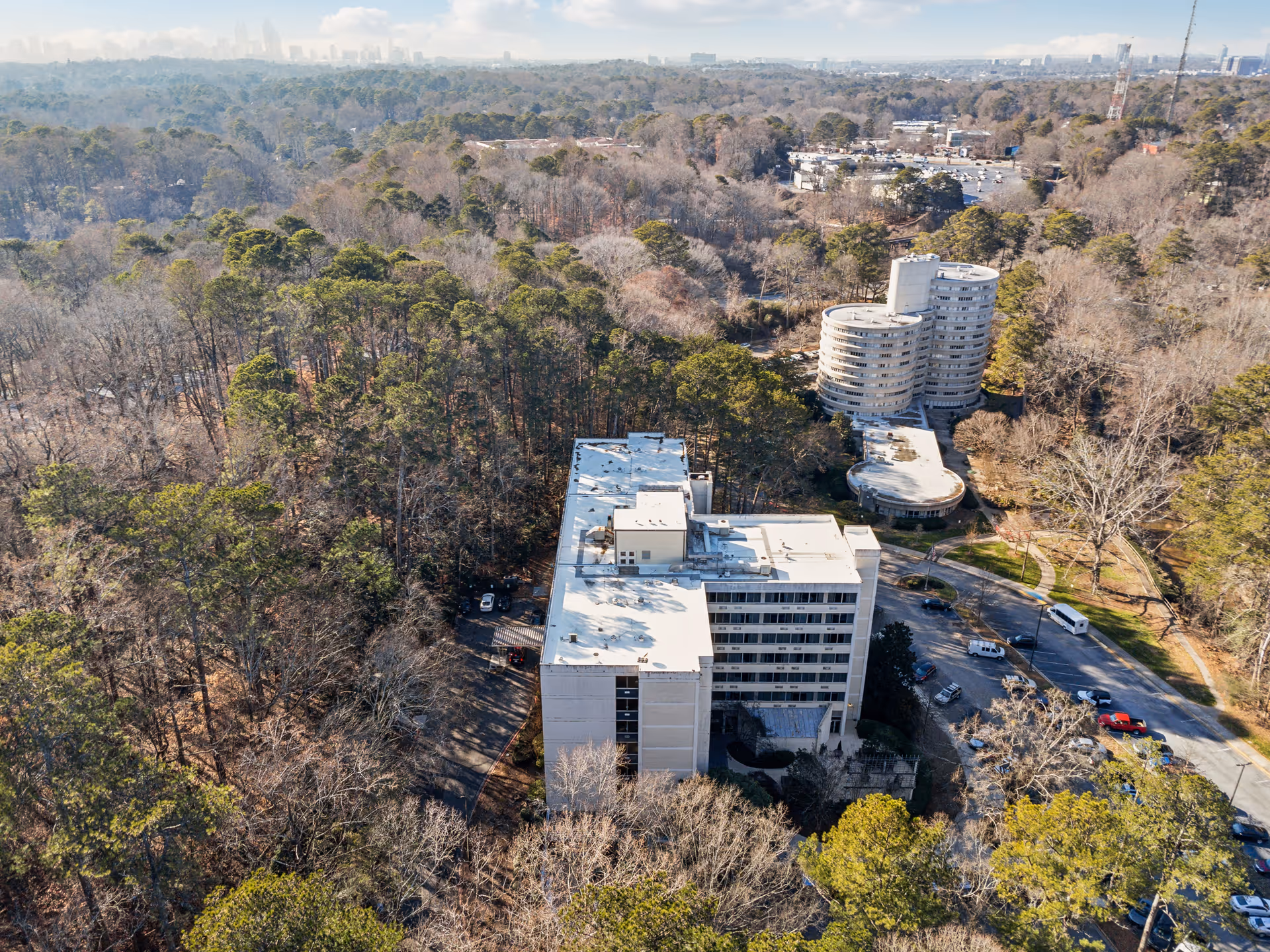 Aerial view of Parkside at Budd Terrace Nursing & Rehab Center surrounded by trees and greenery, with multiple buildings and a parking area visible under a partly cloudy sky.