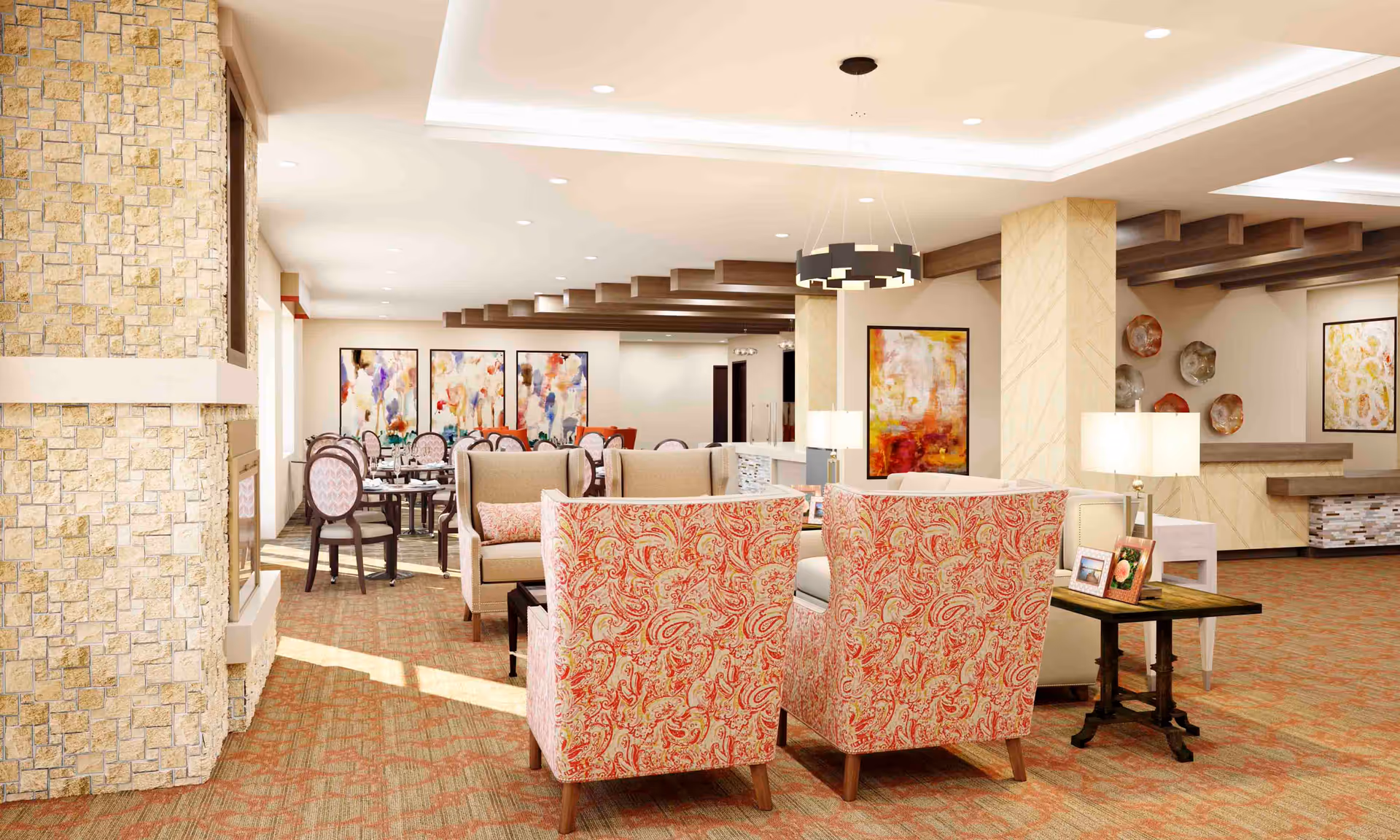A spacious and well-lit common area in a senior living facility featuring comfortable seating with patterned armchairs and sofas arranged around a coffee table. The room has a stone fireplace on the left, decorative wall art, and a dining area with tables and chairs in the background. The ceiling has recessed lighting and wooden beams, and there are lamps on side tables providing additional light.