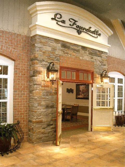 Decorative stone-and-brick interior entrance with open double doors beneath a sign reading "La Fourchette".
