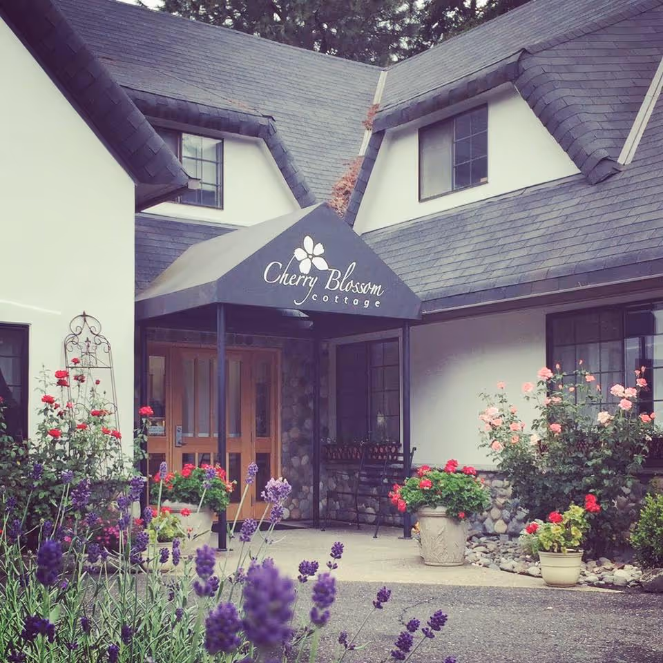 Entrance of a cottage-style building with a black awning reading 'Cherry Blossom Cottage', potted flowers and lavender in the foreground.