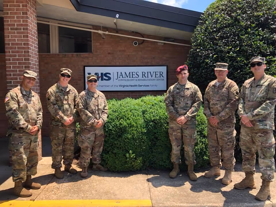 Seven uniformed service members standing outside the James River Convalescent & Rehabilitation Center next to the facility sign.