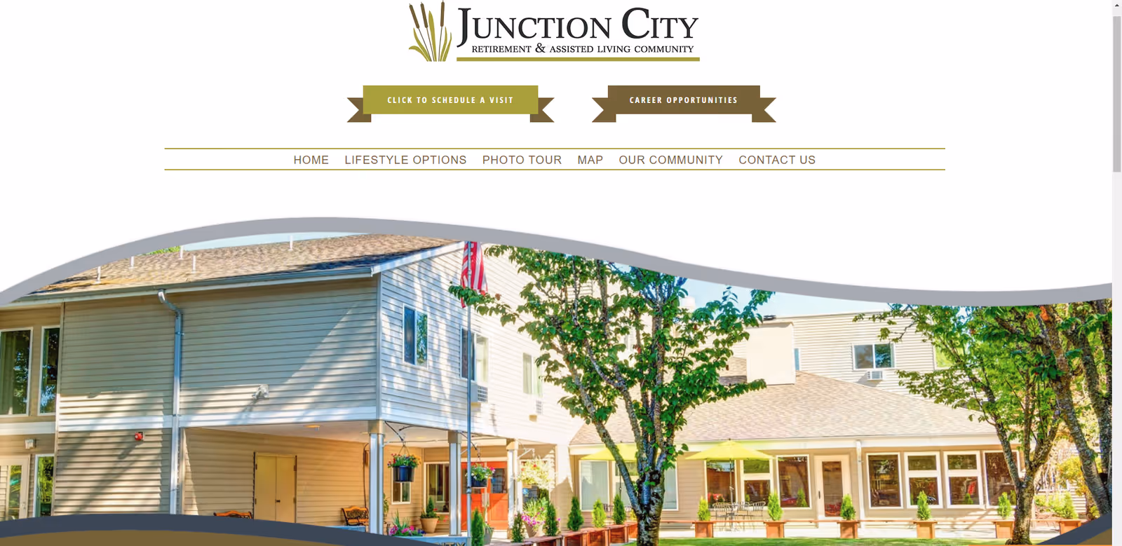 Exterior view of Junction City Retirement and Assisted Living community building with trees and outdoor seating area under a sunny sky.