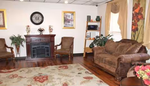 Miller's Merry Manor living room with fireplace, brown leather seating, rug, plants, and art.