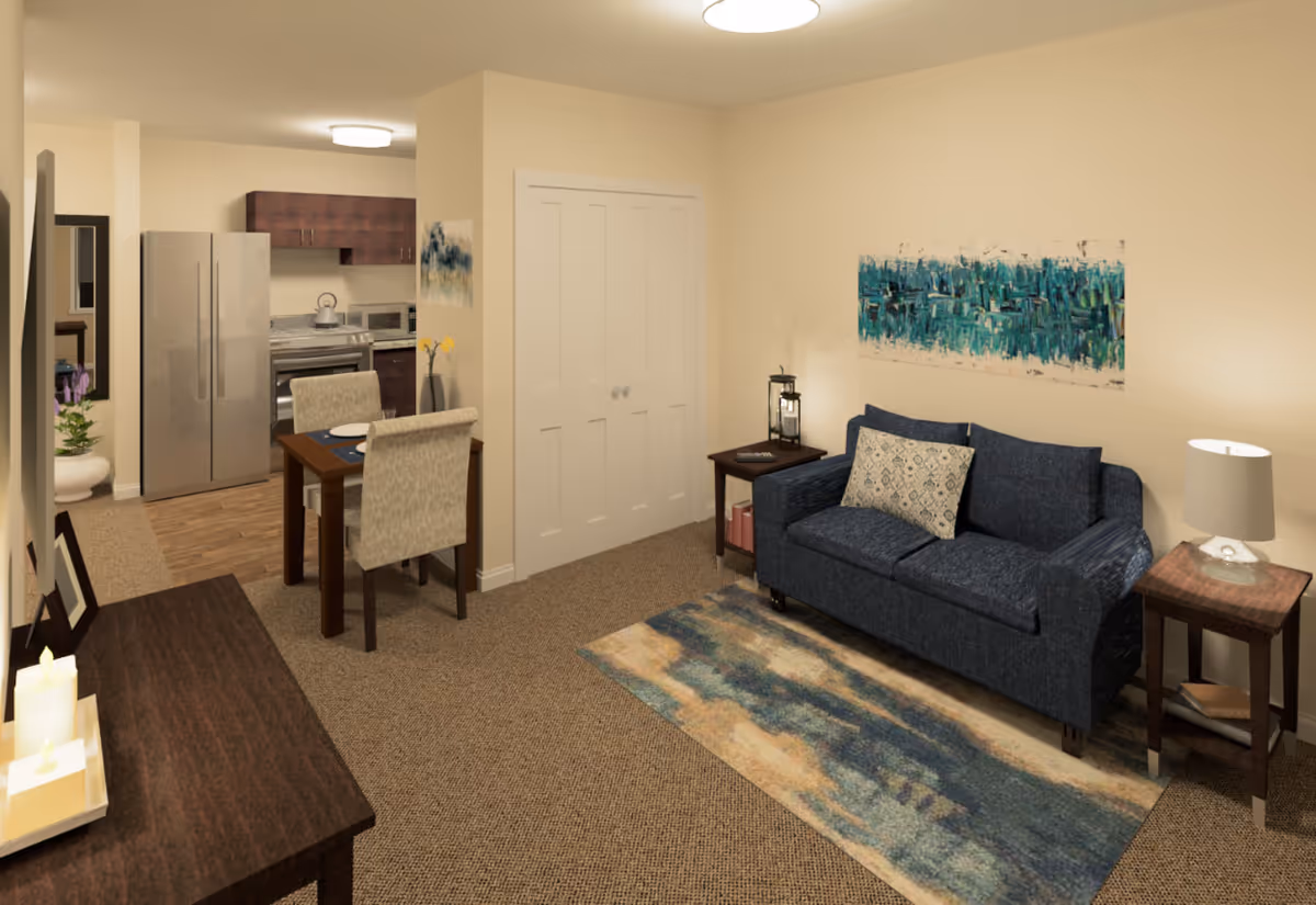 Open-plan interior showing a navy loveseat with side tables and rug, a small dining table, and a kitchenette in the background.