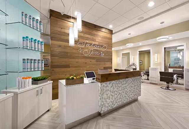 Stylish salon and spa reception area with a wood accent wall, front desk, product shelves, and styling chairs.