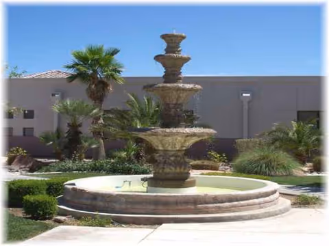 Multi-tier stone fountain in a sunny courtyard with palms and landscaping.