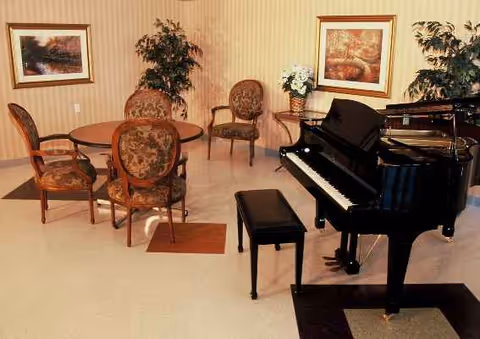 Beige-walled lounge with a black grand piano, round table, and upholstered chairs.