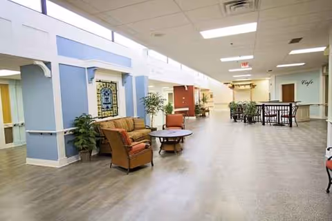 Spacious indoor senior living lobby with chairs, plants, and a coffee cafe.