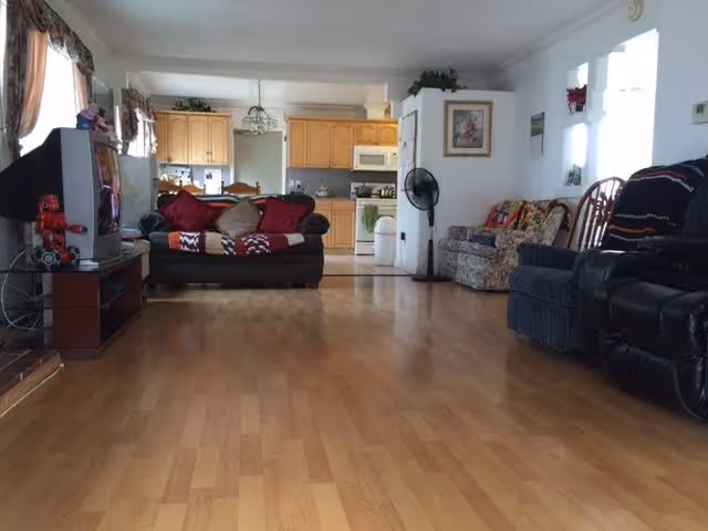 Spacious living room with wooden floor, several couches, TV, and a kitchen in the background.