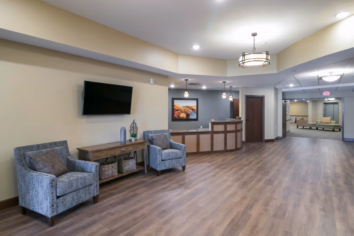 Spacious reception lobby with two upholstered chairs, a console table and wall-mounted TV facing a curved reception desk.