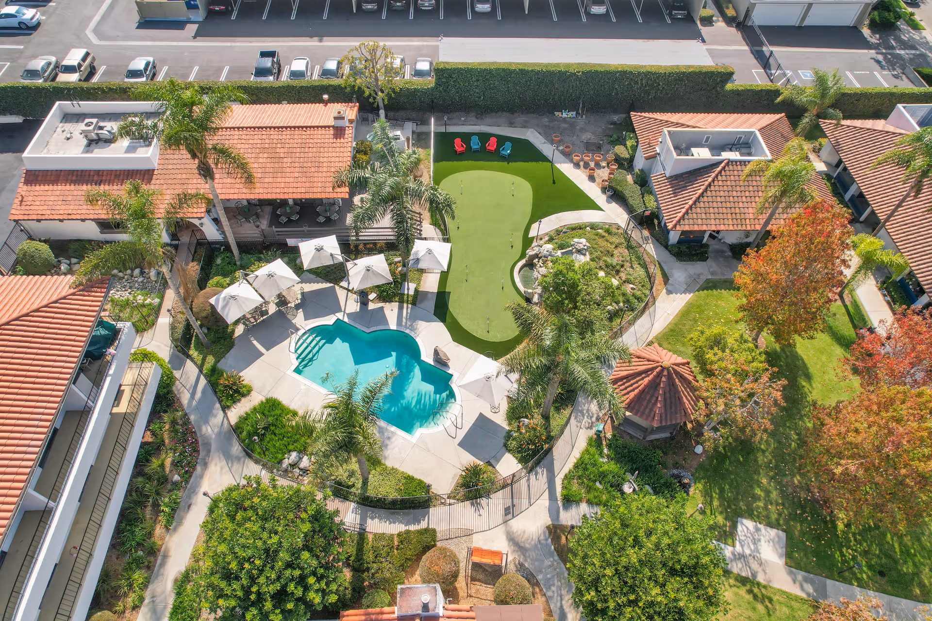 Aerial view of a courtyard at Huntington Terrace with a swimming pool, putting green, palm trees, umbrellas, and red-tiled buildings.