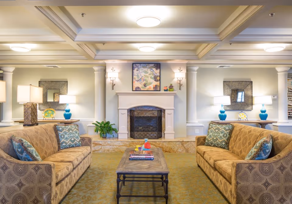 Well-lit lounge with two patterned sofas facing a coffee table and a fireplace beneath coffered ceilings.