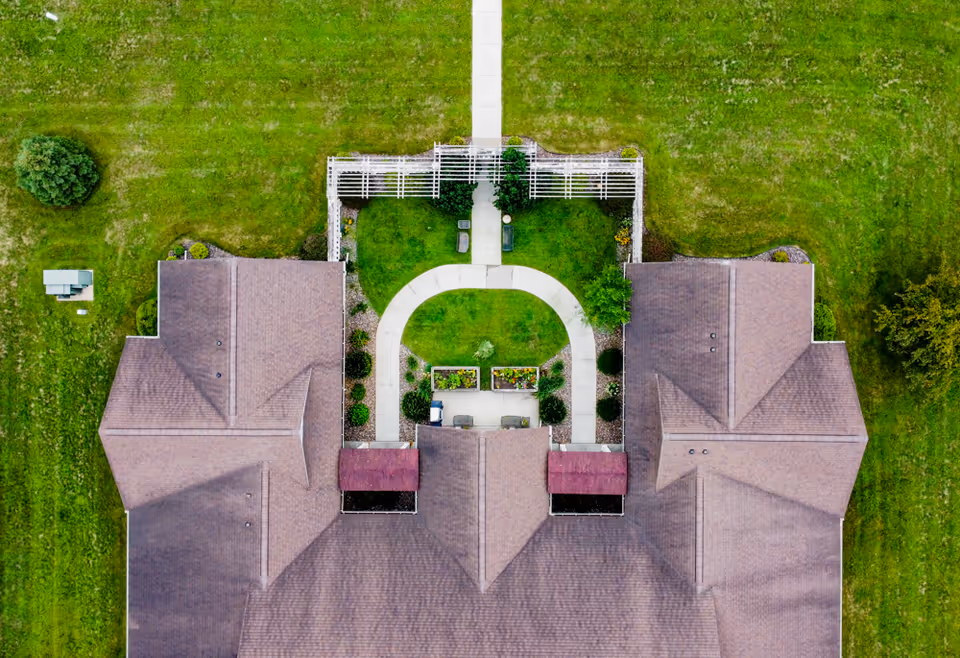 Aerial top-down view of a senior living facility showing symmetrical rooftops and a central landscaped courtyard with curved walkways, raised planters, and a pergola.