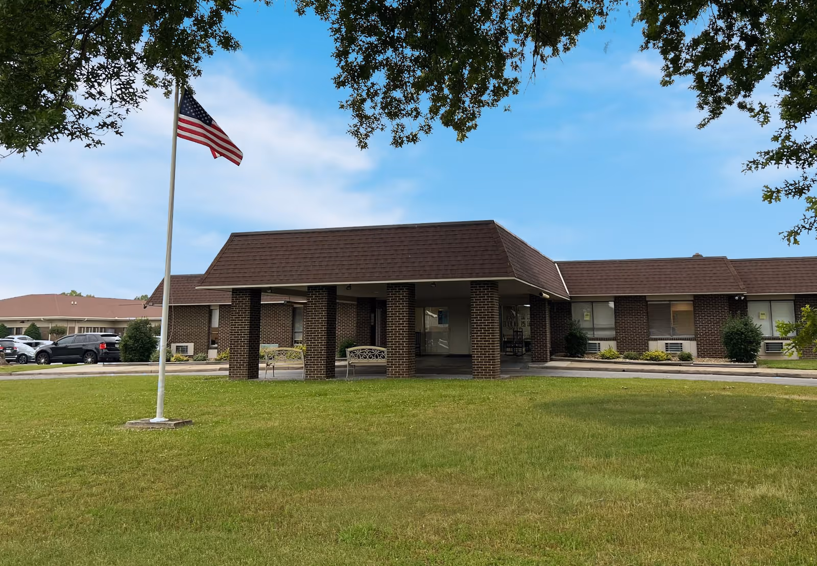 Brick building with a porte-cochere entrance, flagpole, and green lawn.