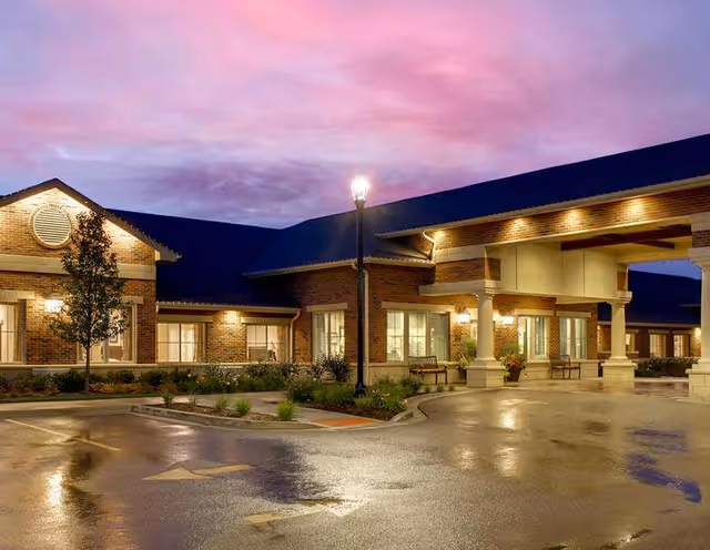 Dusk-lit exterior view of Maple Glen Memory Care Community with covered entrance and parking.