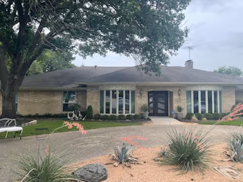Single-story brick building with a central entrance, large windows, circular driveway, and desert-style landscaping.