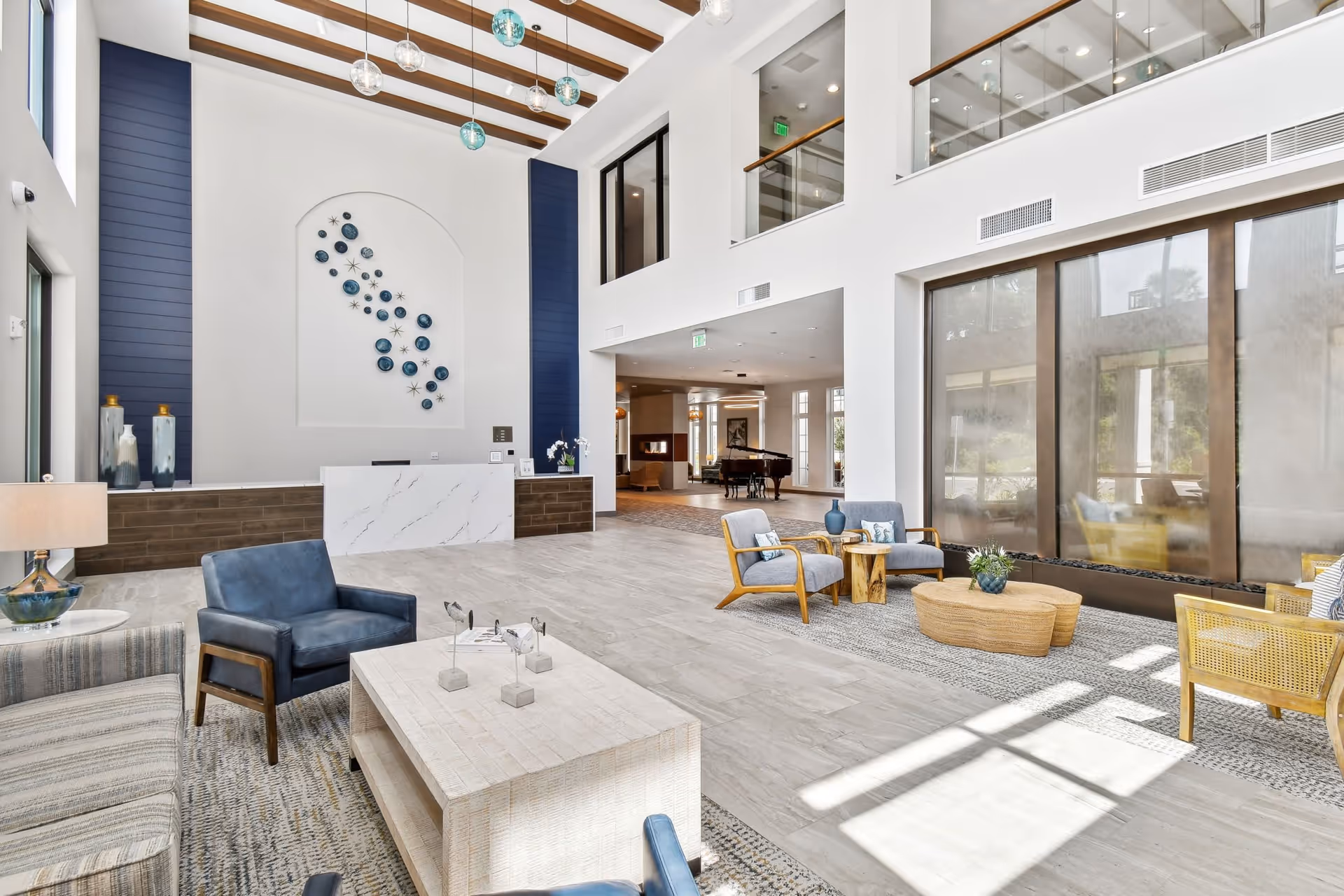 Bright two-story senior living lobby with a reception desk, multiple seating areas, and large windows.