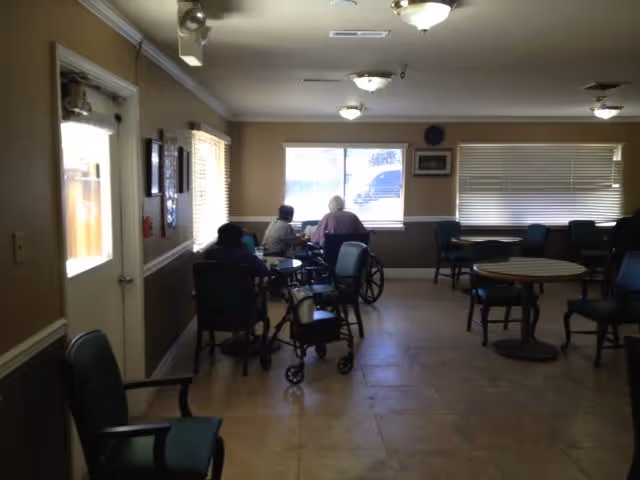 Interior common room with tables and chairs and a few elderly residents seated near a window
