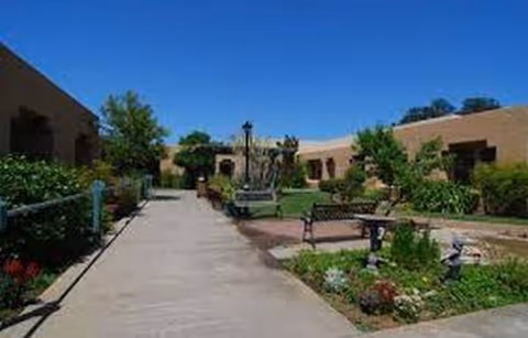 Sunny outdoor courtyard of a post-acute facility, featuring benches, pathways, and landscaped gardens.
