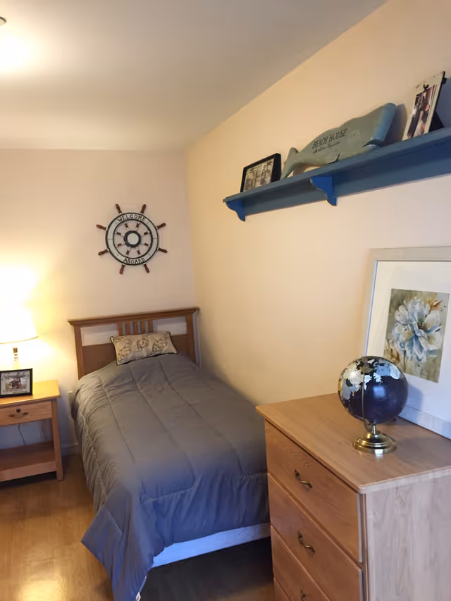 Small bedroom with a single bed, nightstand, dresser, globe, wall shelf and nautical wall decor.