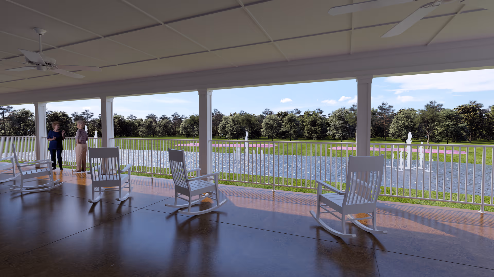 Covered outdoor patio area with white rocking chairs facing a pond with fountains and a grassy area with trees in the background. Two people are standing near the railing, enjoying the view.