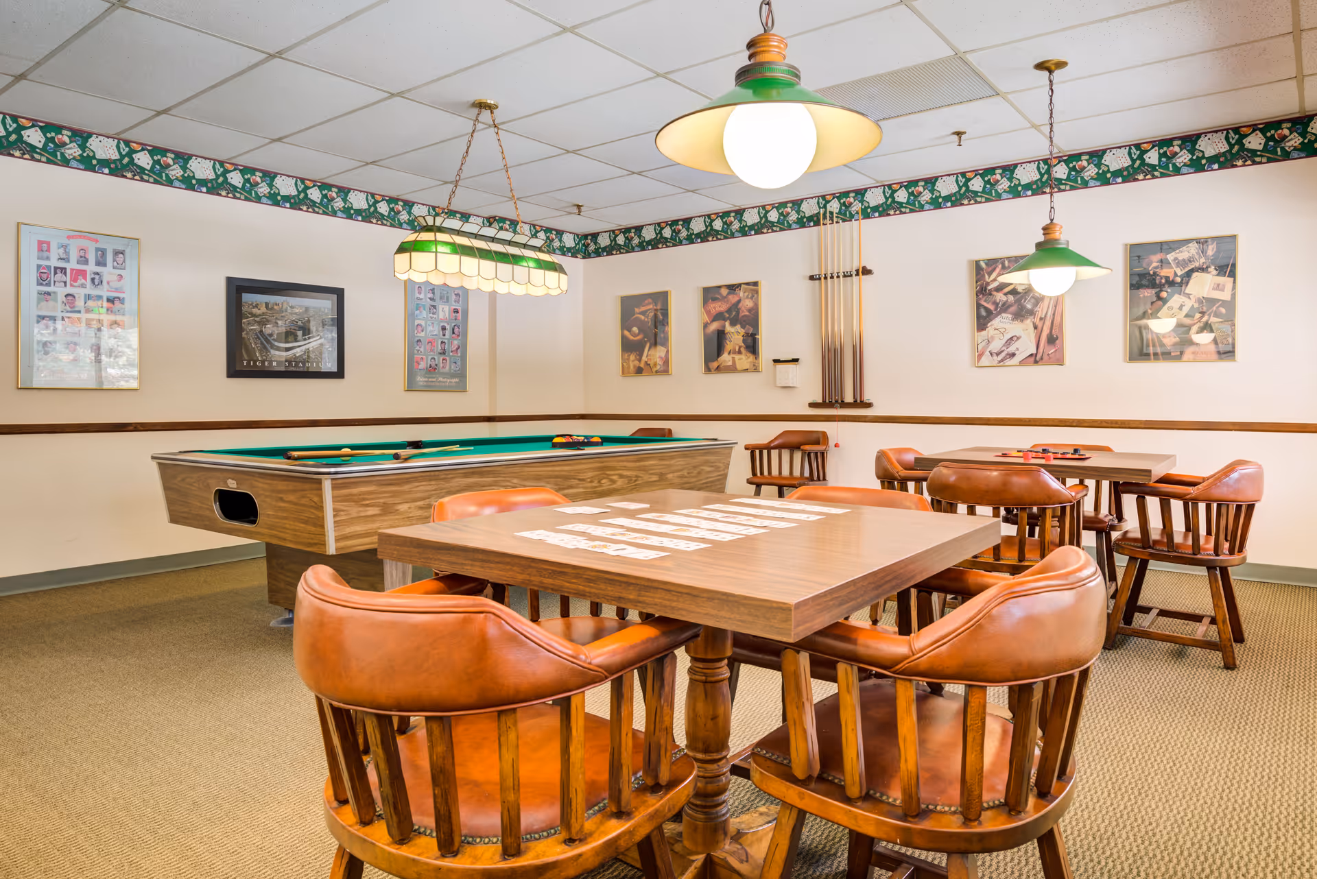 Game room featuring a pool table, card tables and leather wooden chairs under hanging green pendant lights.