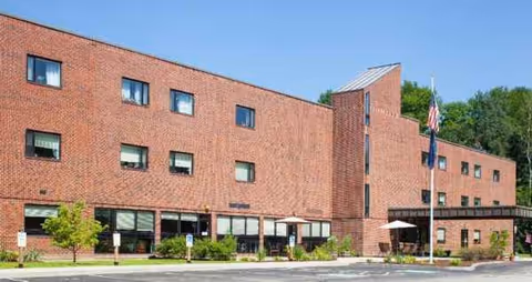 Brick senior living center with multiple windows and an outdoor seating area at the entrance.