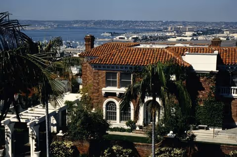 Exterior view of HarborView Senior Assisted Living with red-tiled roof, palm trees, and water.