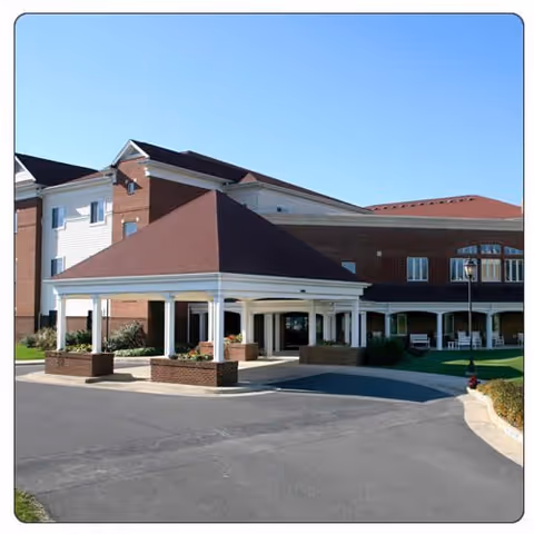 Brick senior living facility with a covered porte-cochere entrance and clear blue sky.