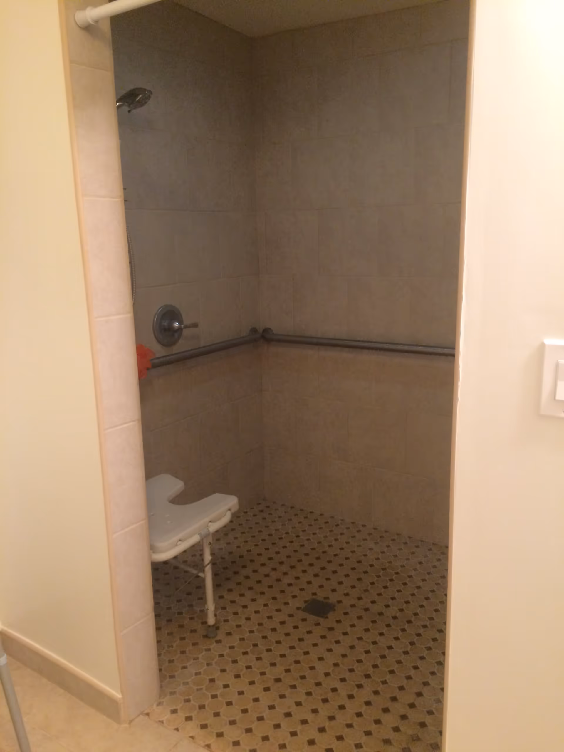 Tiled walk-in shower with grab bars, a showerhead, and a white shower chair.