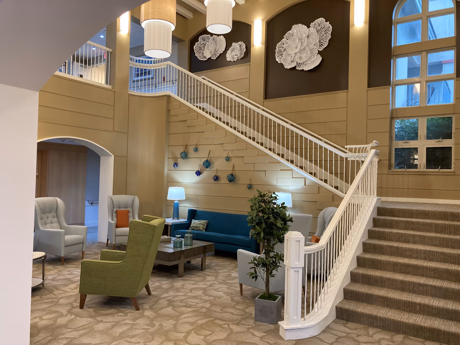 Spacious multi-level lobby with a staircase, seating area of chairs and a sofa, decorative wall art and lamps.