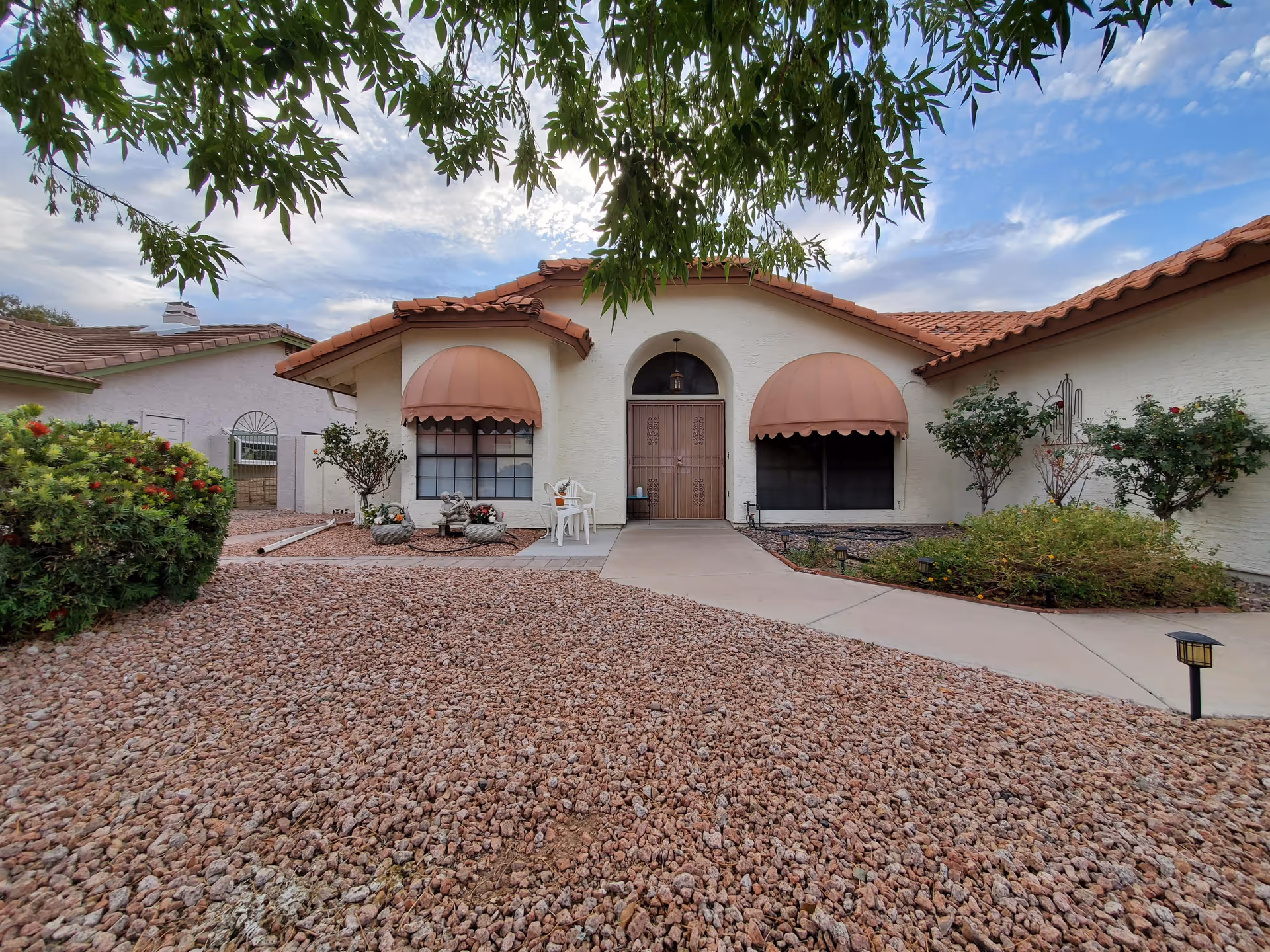 Front entrance of a single-story stucco building with terracotta awnings, a central door, walkway, and gravel desert landscaping.
