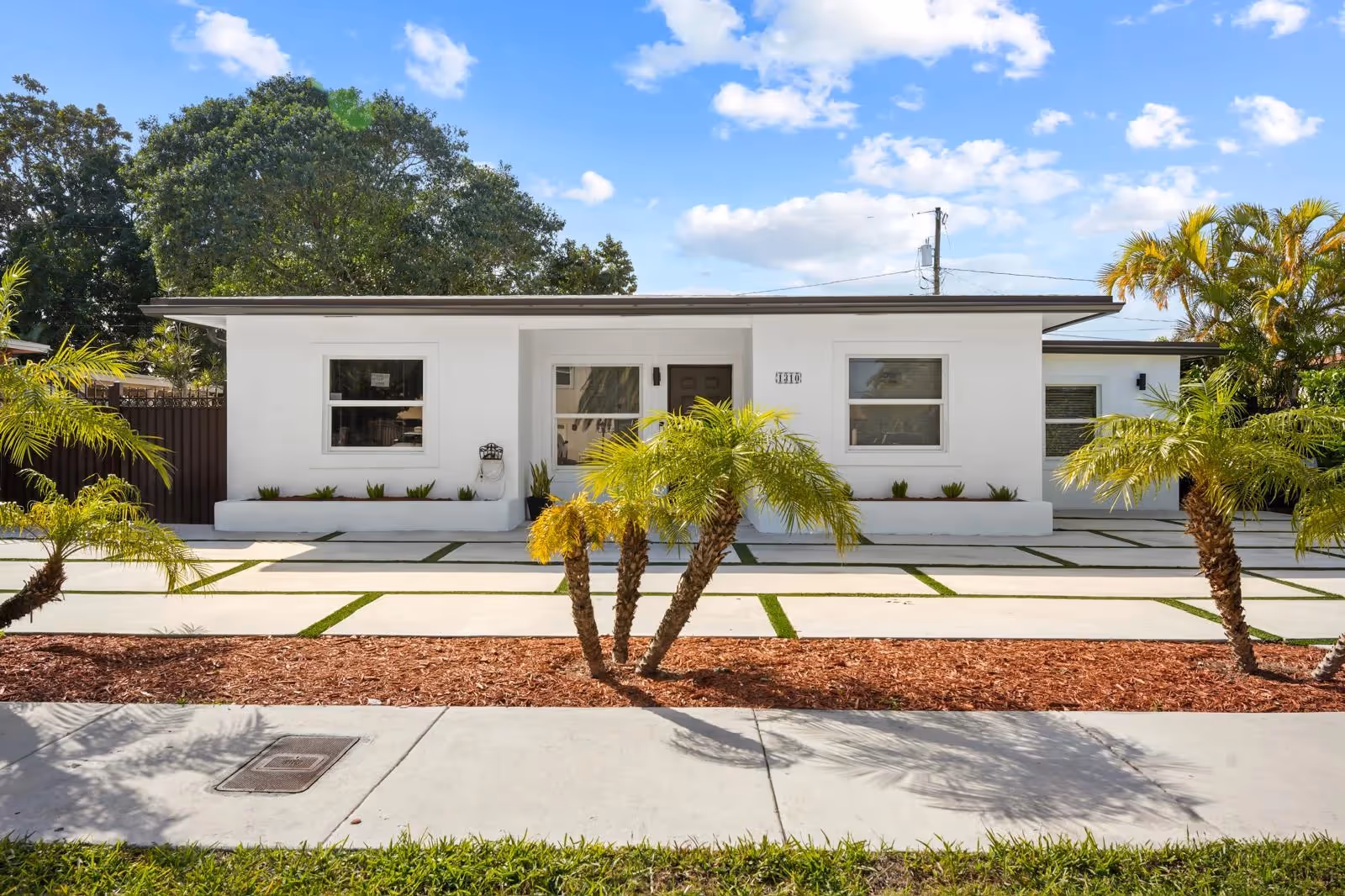 Front exterior of a white, single-story assisted living facility with palm trees and a paved walkway.