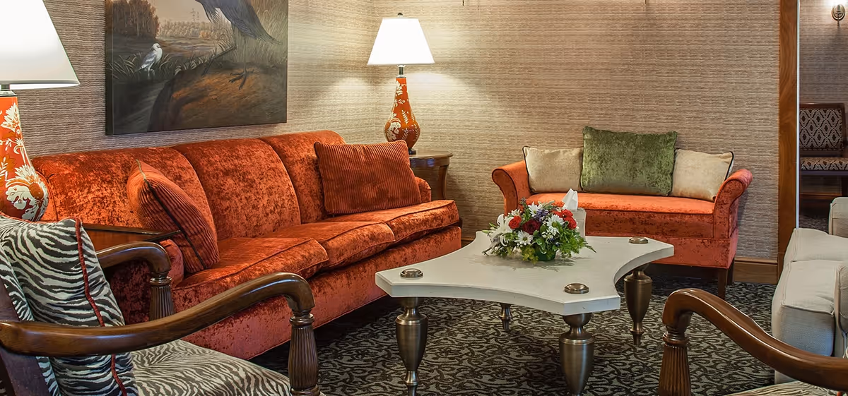 Cozy living room with red velvet sofas and armchairs arranged around a coffee table topped with a floral arrangement and lamps.